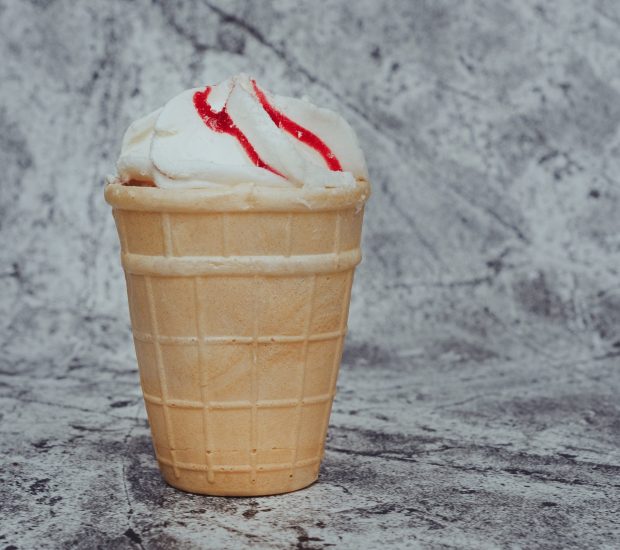 creamy ice cream with strawberry jam in a waffle cup on an abstract gray background